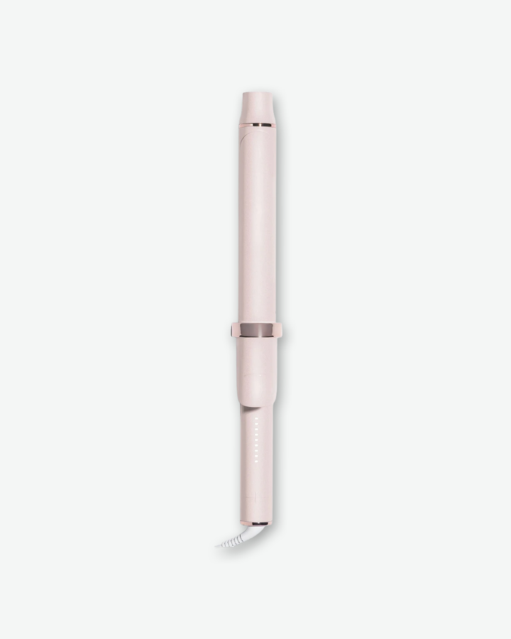 A product shot of a T3 curling iron wand base and barrel, centered vertically against a plain light gray background. The entire interchangeable styling tool is finished in a soft, satin light pink color, accented with a shiny rose-gold ring in the center where the barrel meets the handle grip. Small white LED indicator lights line the lower handle above the white power cord connection.