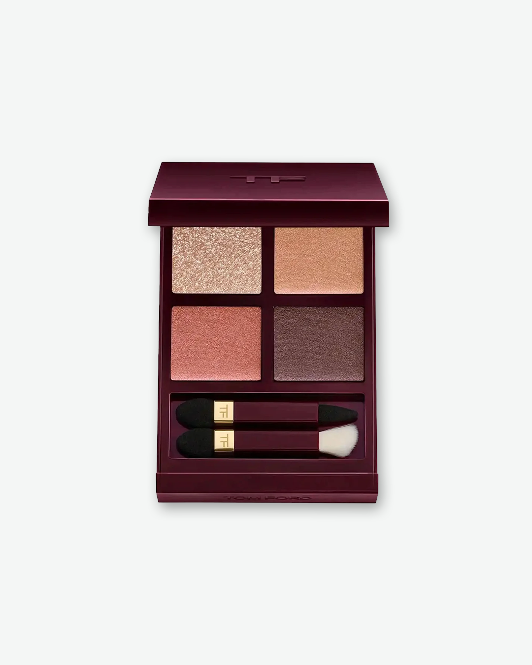 A top-down product shot of an open Tom Ford Eye Color Quad eyeshadow palette, centered against a plain light gray background. The signature deep burgundy and mahogany-toned compact houses four square eyeshadow pans: a shimmering champagne gold (top left), a satin warm peachy gold (top right), a rich shimmering copper rose (bottom left), and a deep satin plum brown (bottom right). Tucked into the lower compartment are two miniature dual-ended eyeshadow applicators detailed with gold bands and the "TF" logo.