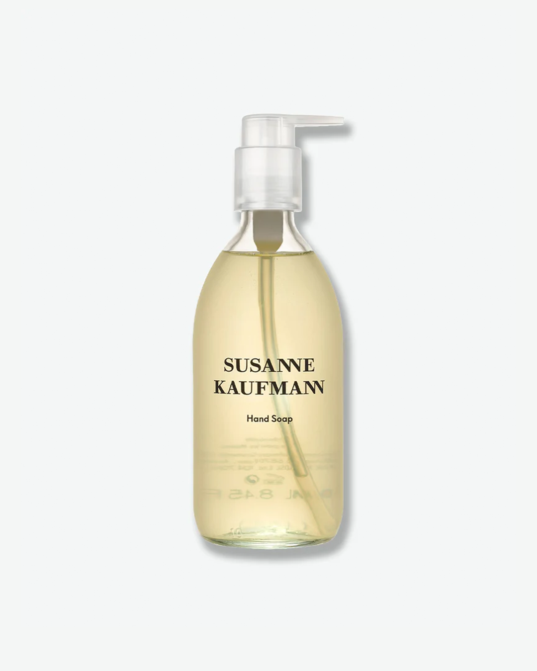 A product shot of a Susanne Kaufmann Hand Soap bottle, centered against a plain light gray background. The curved bottle is made of clear glass, revealing a translucent, light-amber liquid soap inside. It is fitted with a clear plastic pump dispenser and features black text branding on the front.