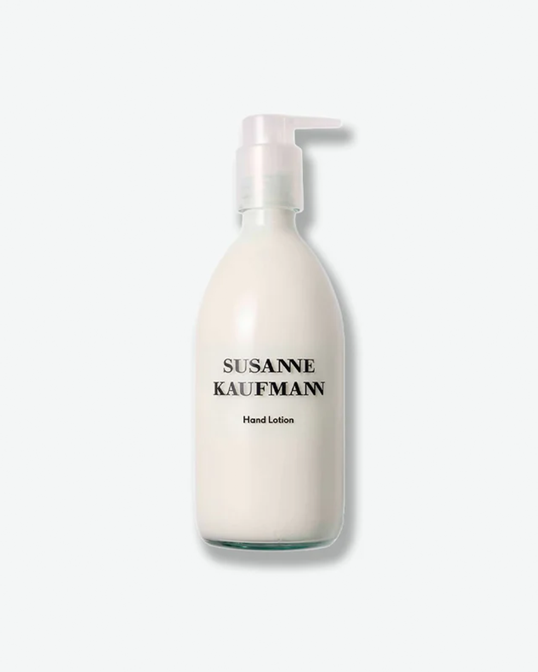 A product shot of a Susanne Kaufmann Hand Lotion bottle, centered against a plain light gray background. The curved bottle is made of frosted clear glass, revealing an opaque white lotion formula inside. It is topped with a clear plastic pump dispenser and displays black text branding on the front.