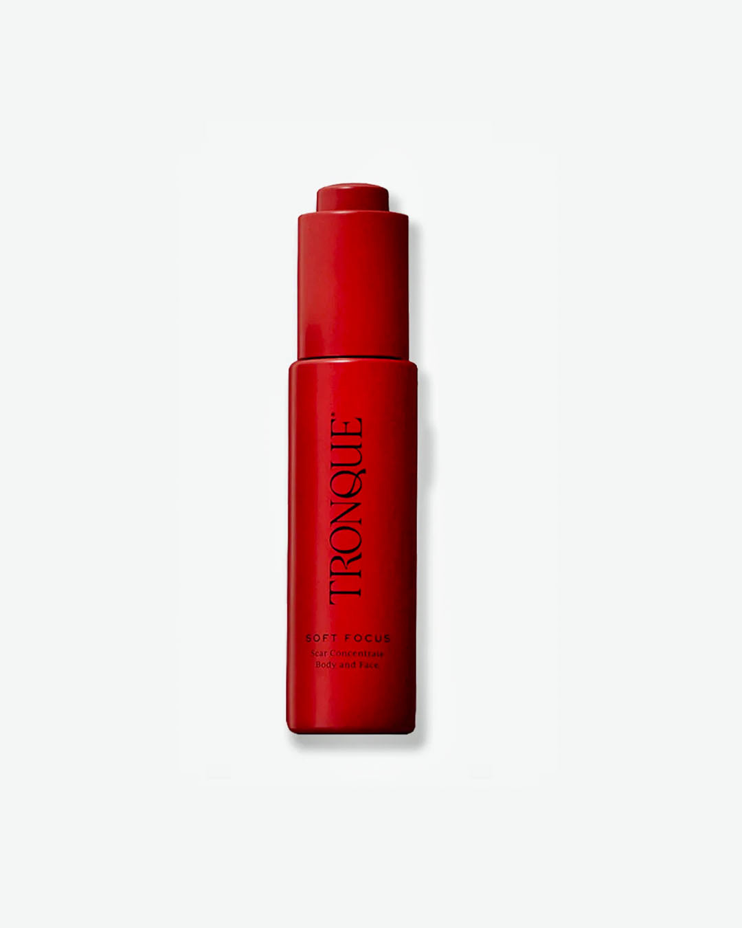 A vertical product shot of Tronque Soft Focus Scar Concentrate for Body and Face. The tall, slim cylindrical bottle is a uniform matte crimson red, topped with an integrated dropper mechanism, with the brand name running vertically in black text.