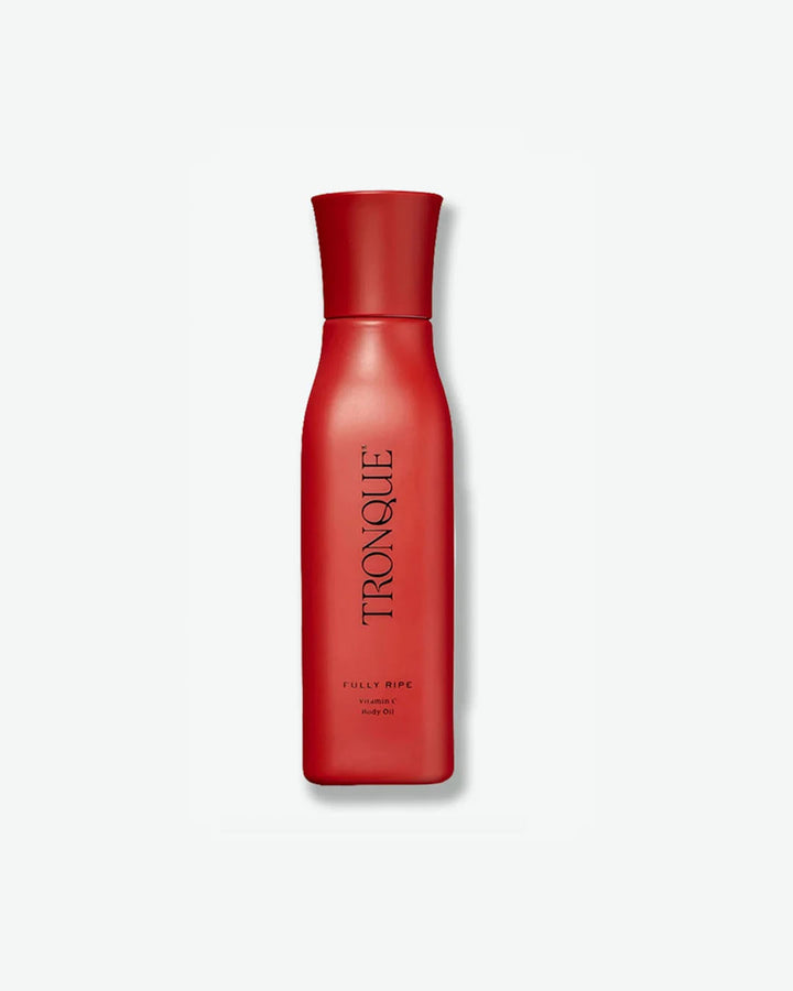 A vertical product shot of Tronque Fully Ripe Vitamin C Body Oil. The bottle features a distinct silhouette that tapers slightly toward a flared cap, finished entirely in a matte crimson red. The brand name is printed vertically down the center in a clean black font.