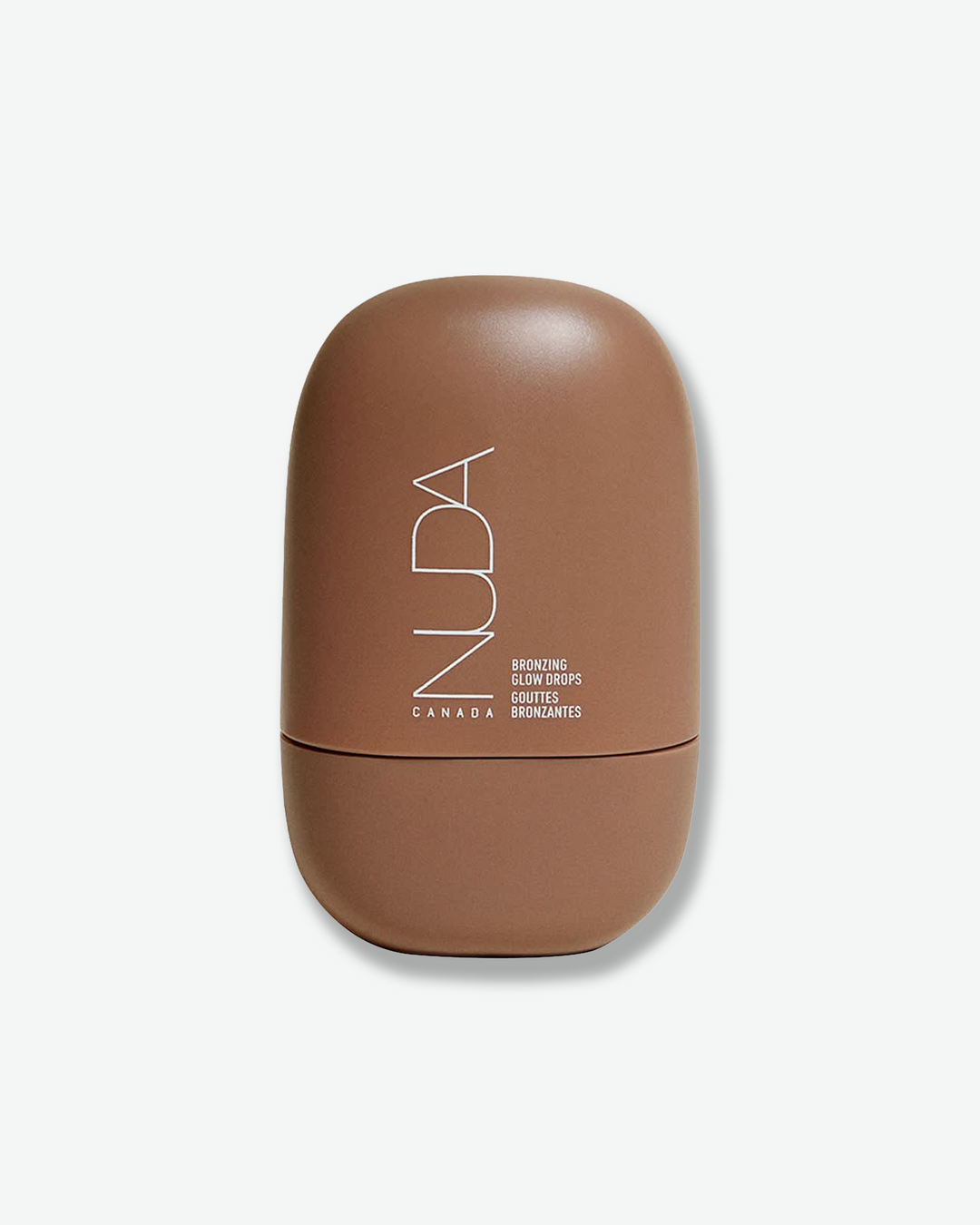 Front view of a NUDA Bronzing Glow Drops container centered against a plain gray background. The modern, pebble-shaped bottle has a matte, warm medium-brown finish and features the brand name "NUDA" printed vertically in a thin white font alongside the product details.