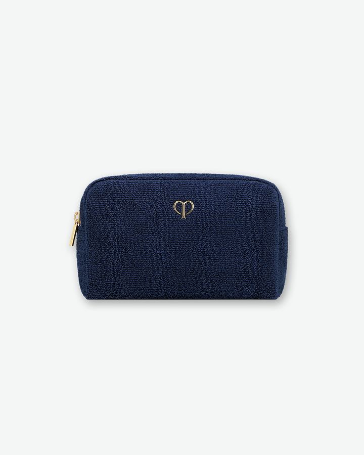 A textured, dark navy blue cosmetic pouch by Clé de Peau Beauté, centered on a solid white background. The pouch is rectangular with rounded top corners, made from a soft bouclé or terry cloth fabric, and features a minimalist, metallic gold brand logo in the center with a matching gold zipper on the left side.