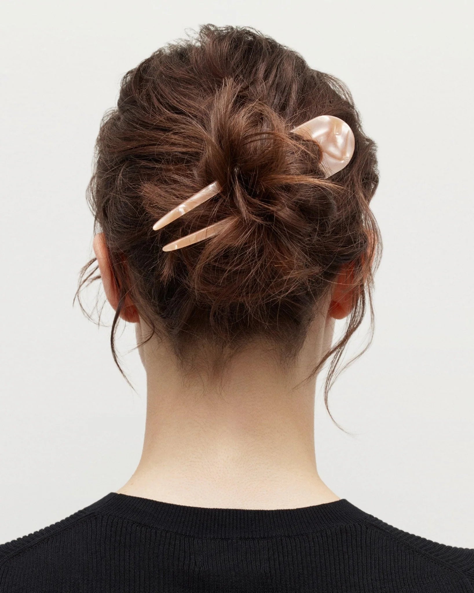 Back view of a person with a stylish hair bun using hair clips on a plain background