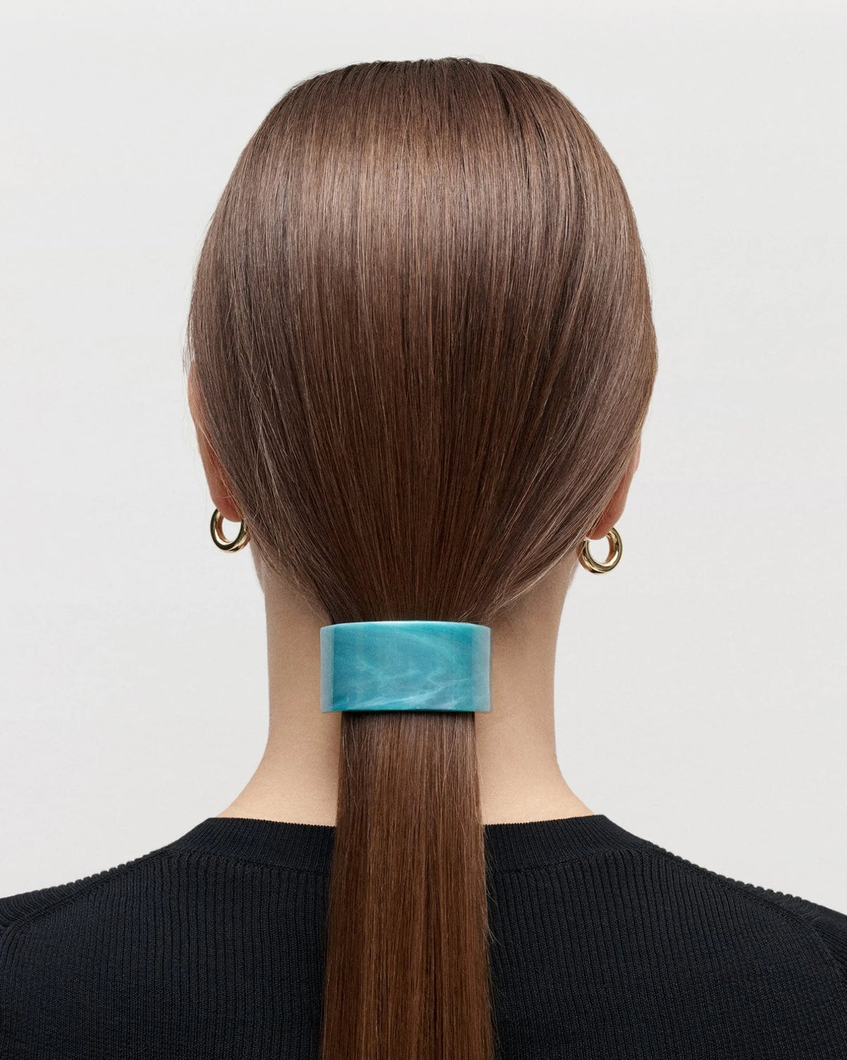 Person with a high ponytail wearing a turquoise scrunchie on a plain background