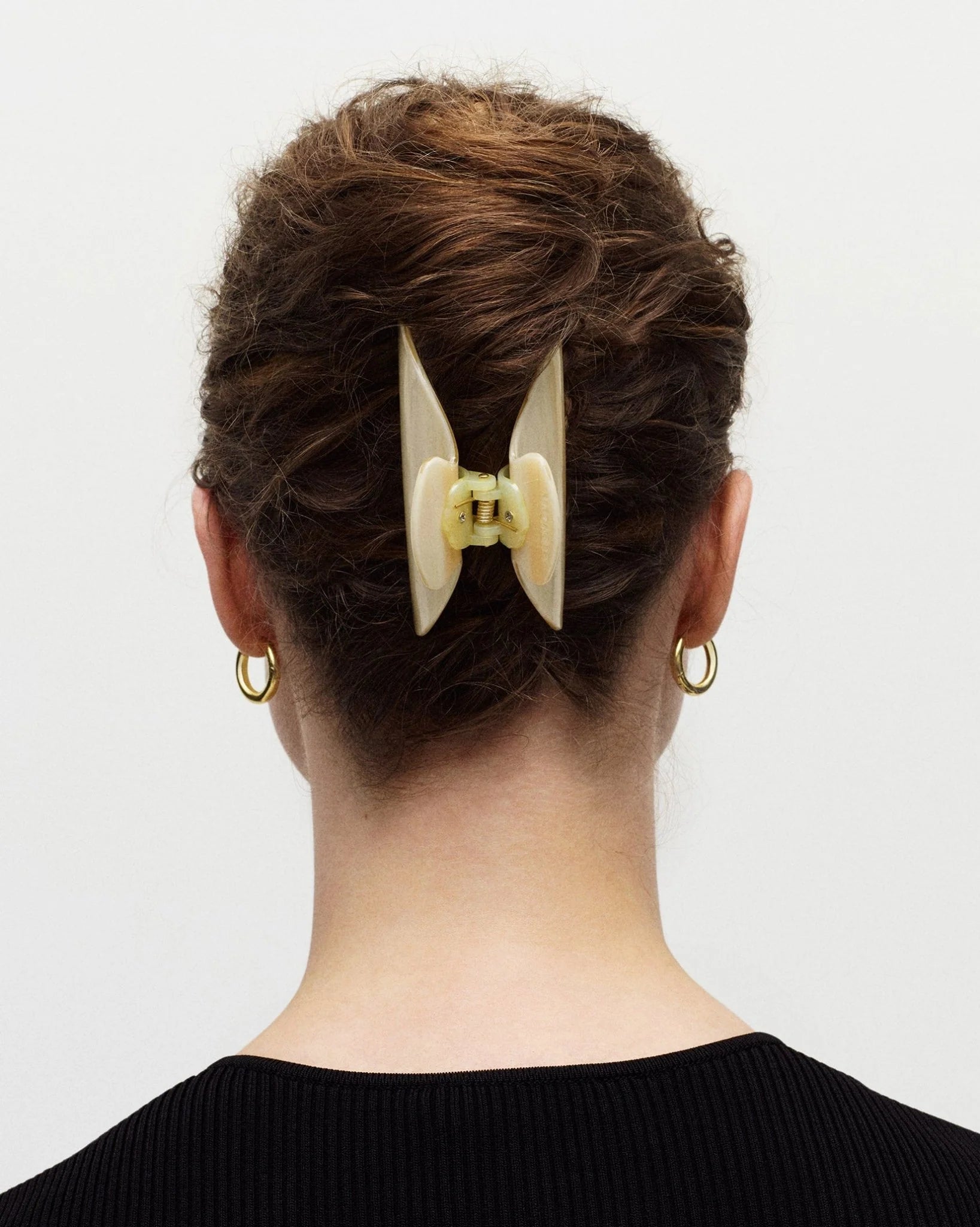 Person with a stylish hair bun featuring a large beige hair clip on a plain background
