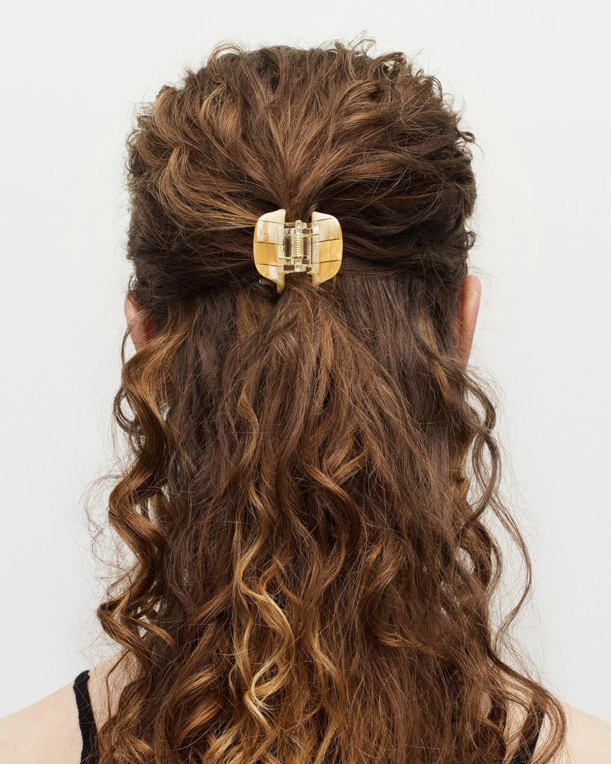 Woman with wavy hair wearing a gold hair clip on a white background