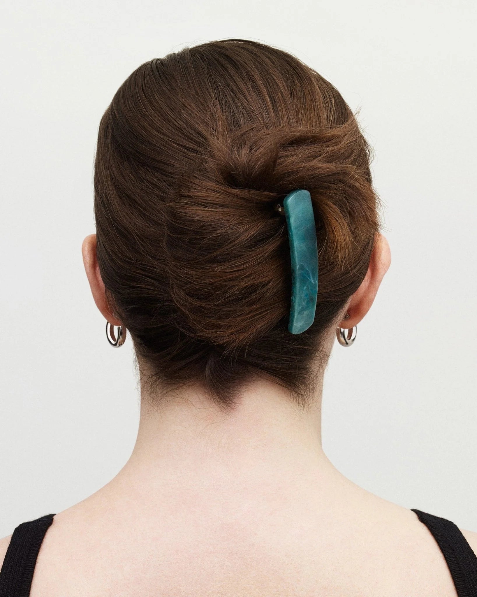 Person with a teal hair clip in their bun against a plain background