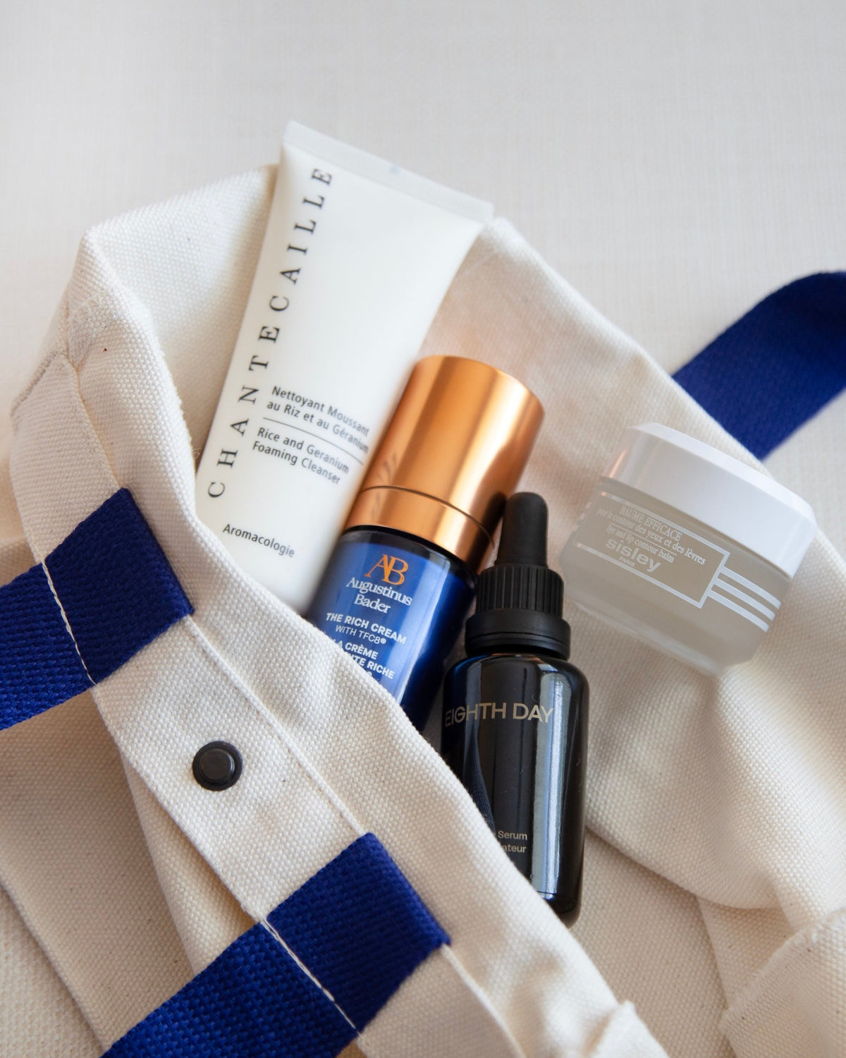 Cos Bar canvas Essentials Tote with blue straps filled with luxury skincare products from Chantecaille, Augustinus Bader, Eighth Day, and Sisley.